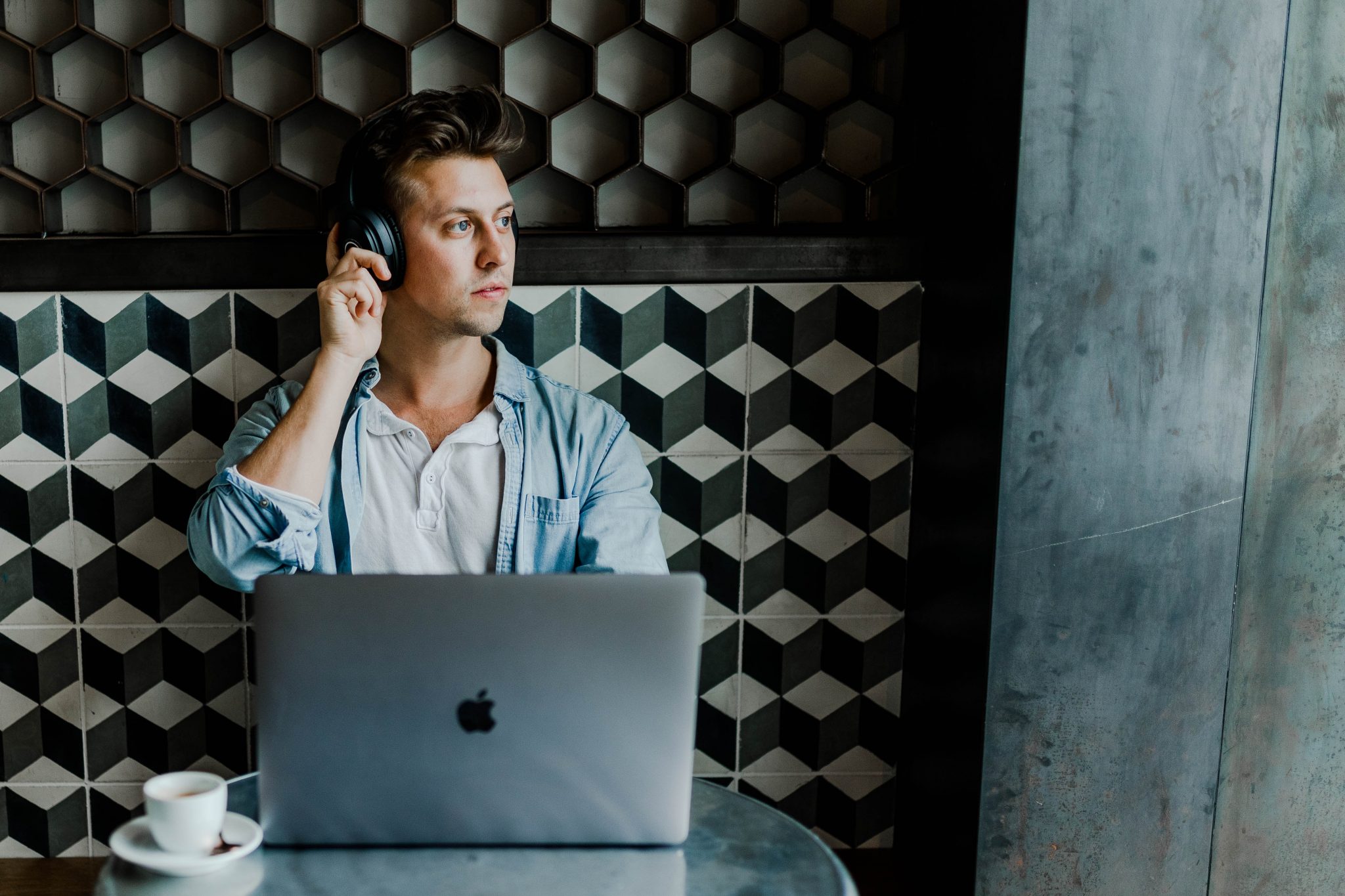 A young man sitting at a table in a cafe listening to music on his Apple Macbook