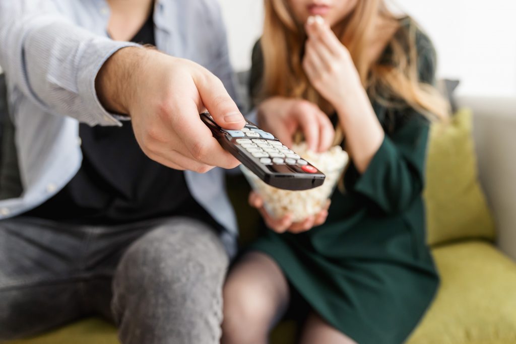 A man and a woman sat on a sofa holding a TV remote